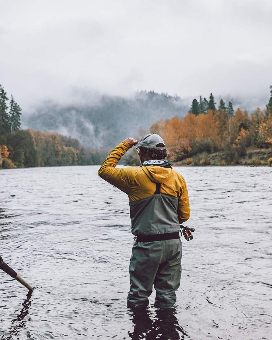 Person standing in water next to a boat on a river with trees and mountains in the background