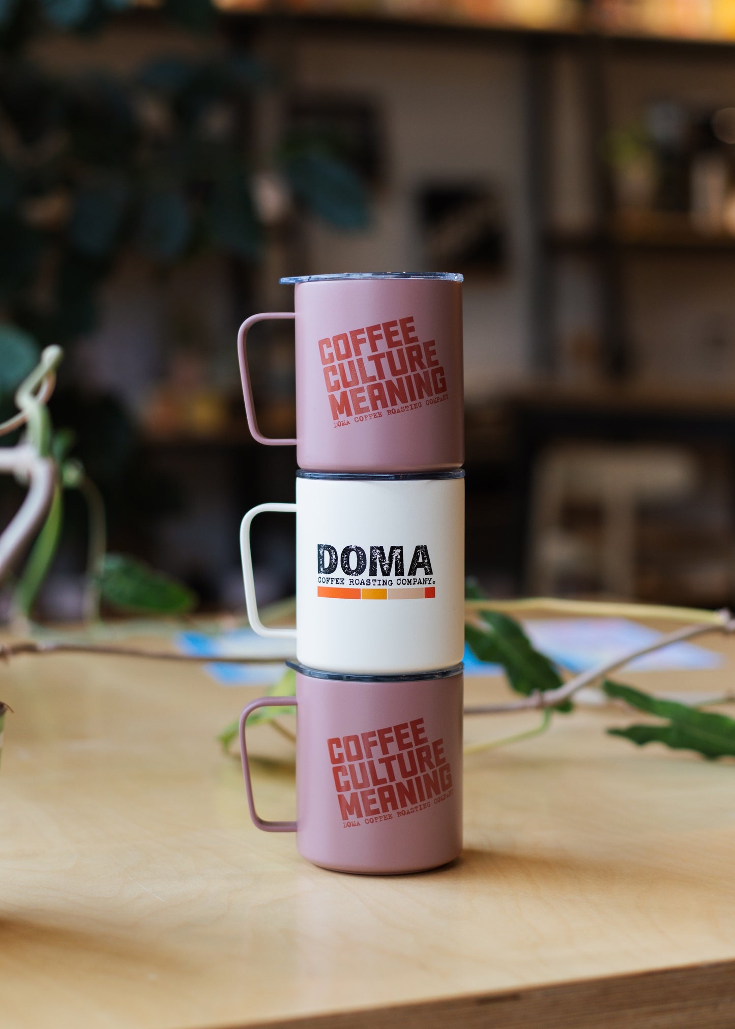 Stack of three DOMA camp mugs on a wooden table.