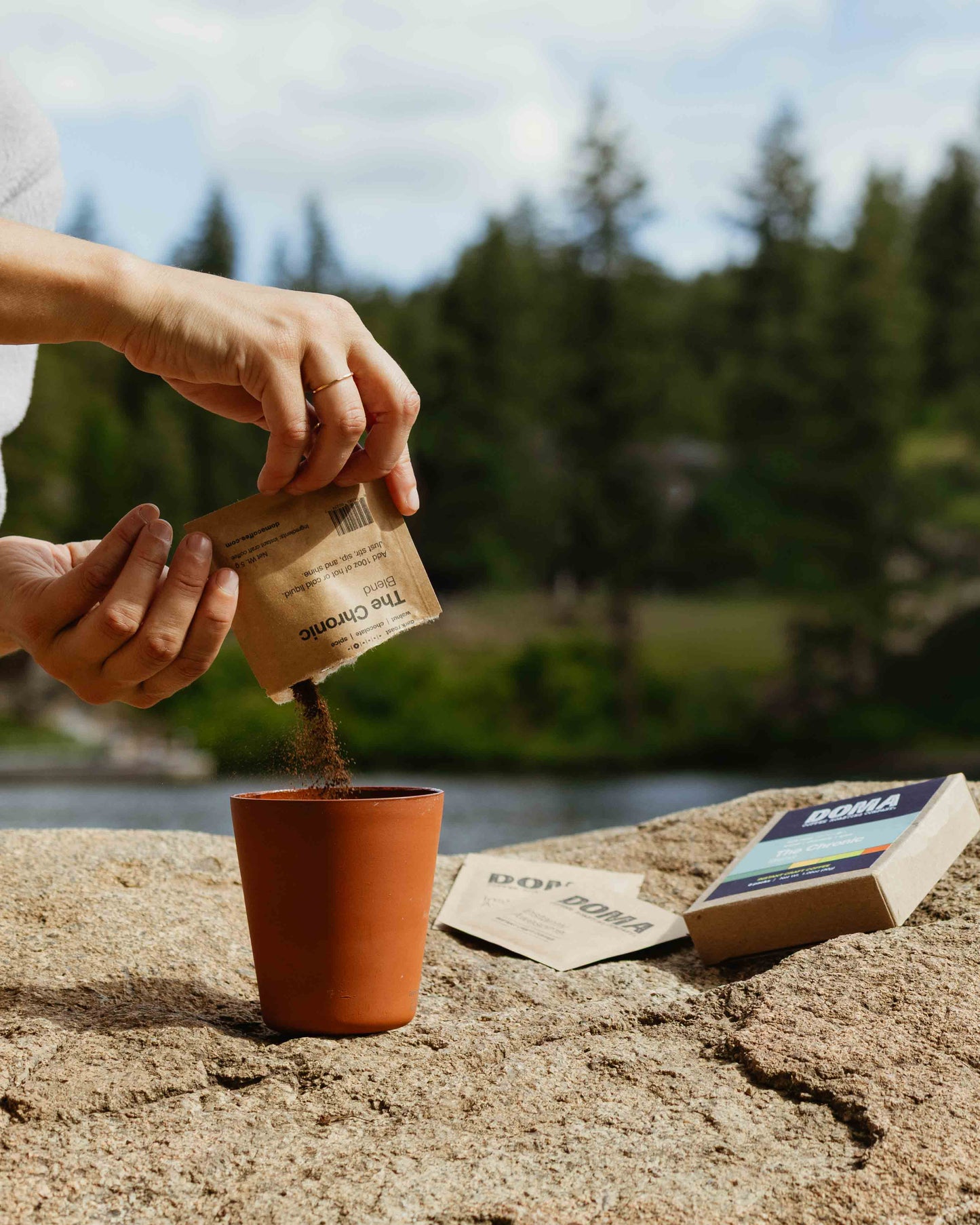 Person pouring coffee grounds into a cup with a scenic river background
