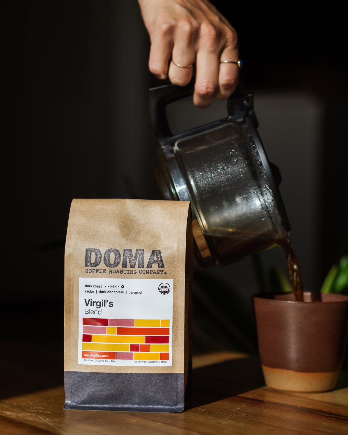 Person pouring coffee into a cup next to a bag of DOMA coffee